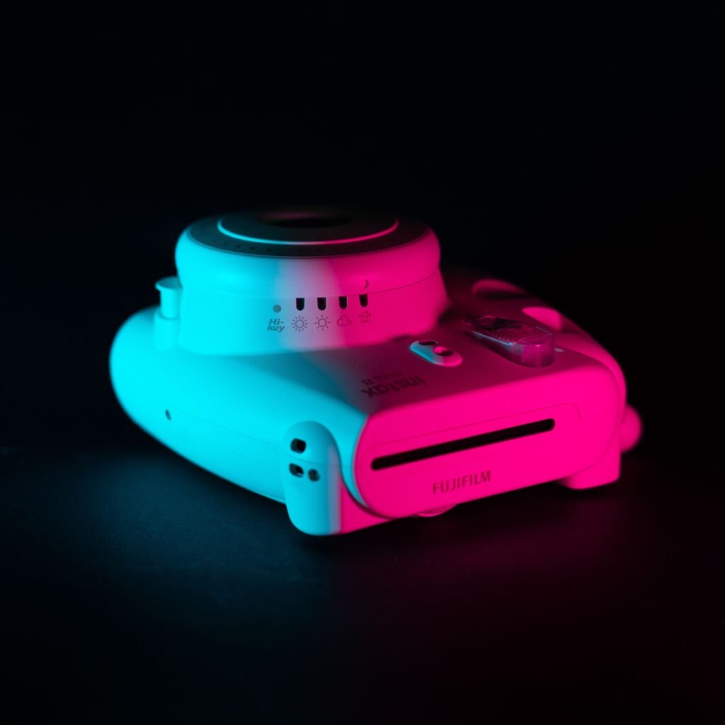 Artistic close-up of an instant camera with dynamic blue and red neon lighting on a black background.